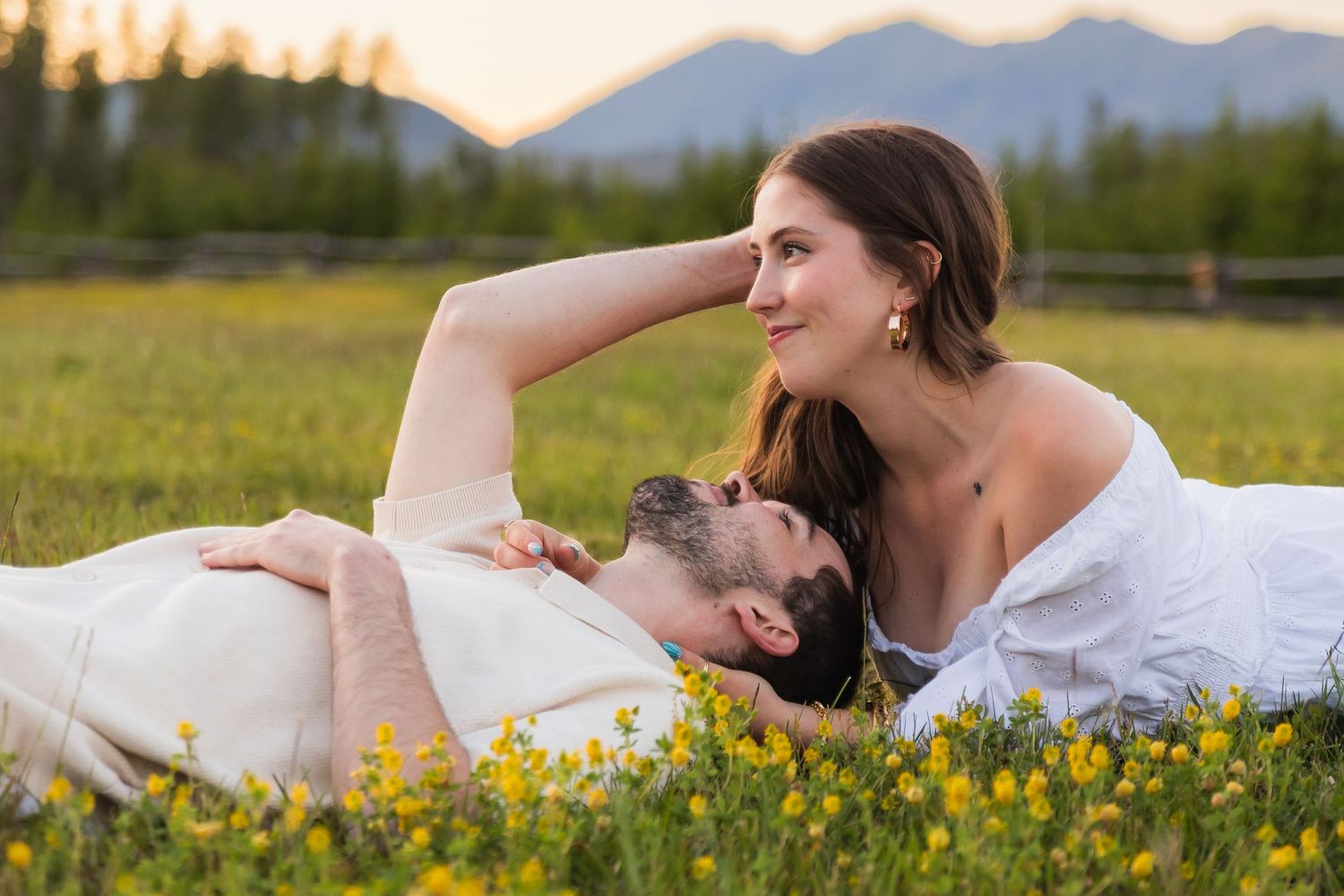Couple lying in a wildflower meadow at sunset with mountains in the background.