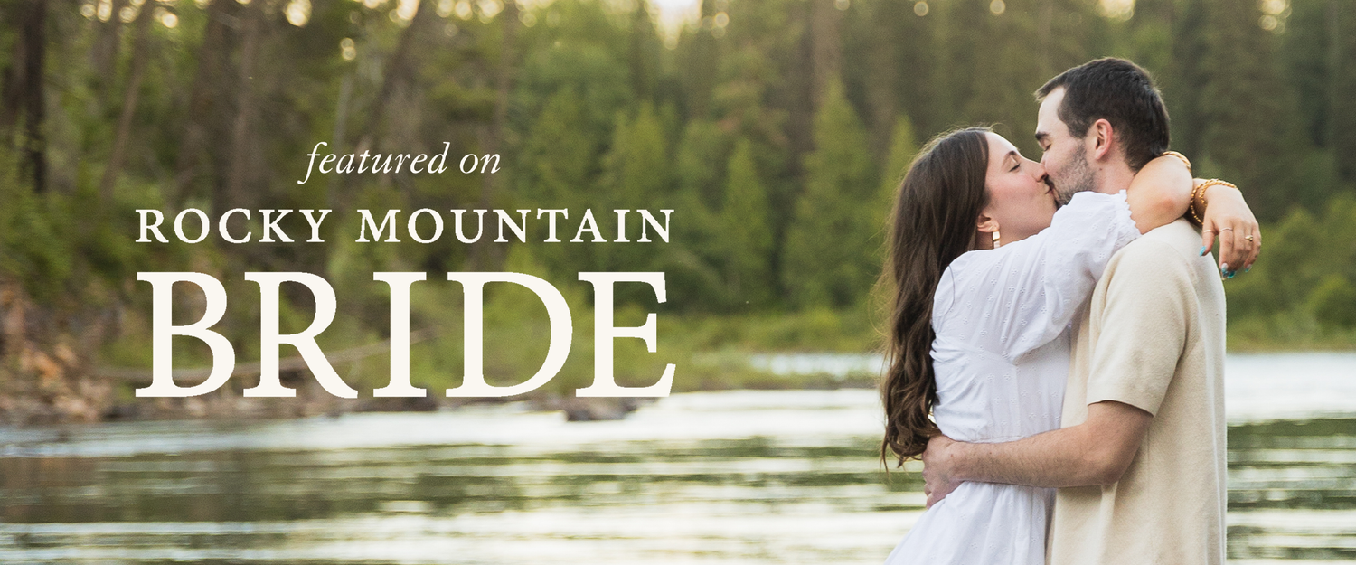 Couple sharing a romantic kiss featured on Rocky Mountain Bride magazine with a scenic river backdrop.