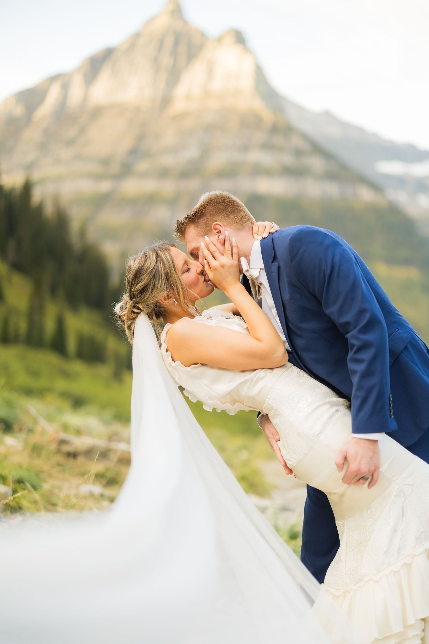 Bride and groom share a romantic dip kiss with a stunning mountain backdrop during their outdoor wedding ceremony.
