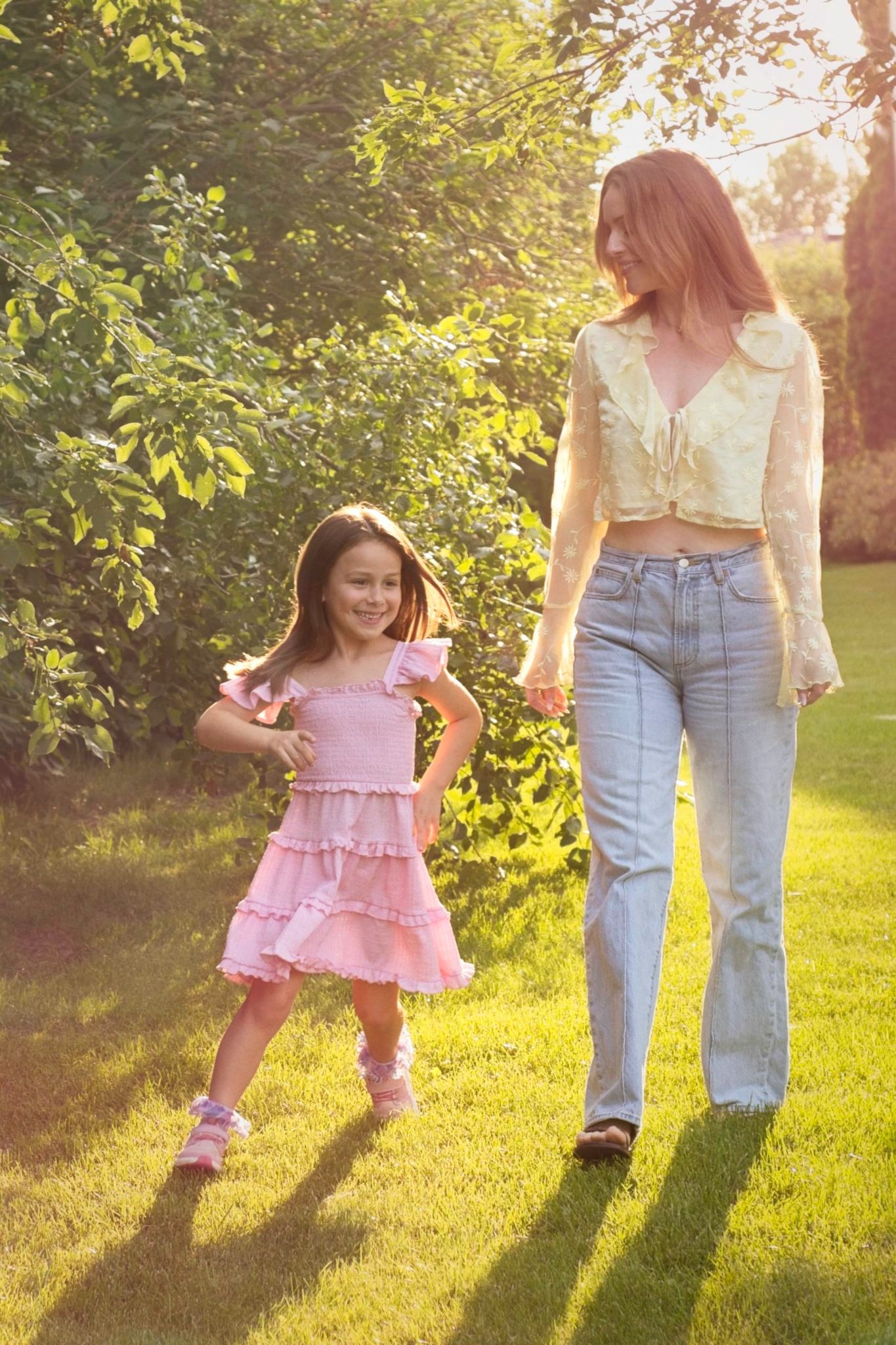 Young child runs around her mother as they walk together in a park during sunset.
