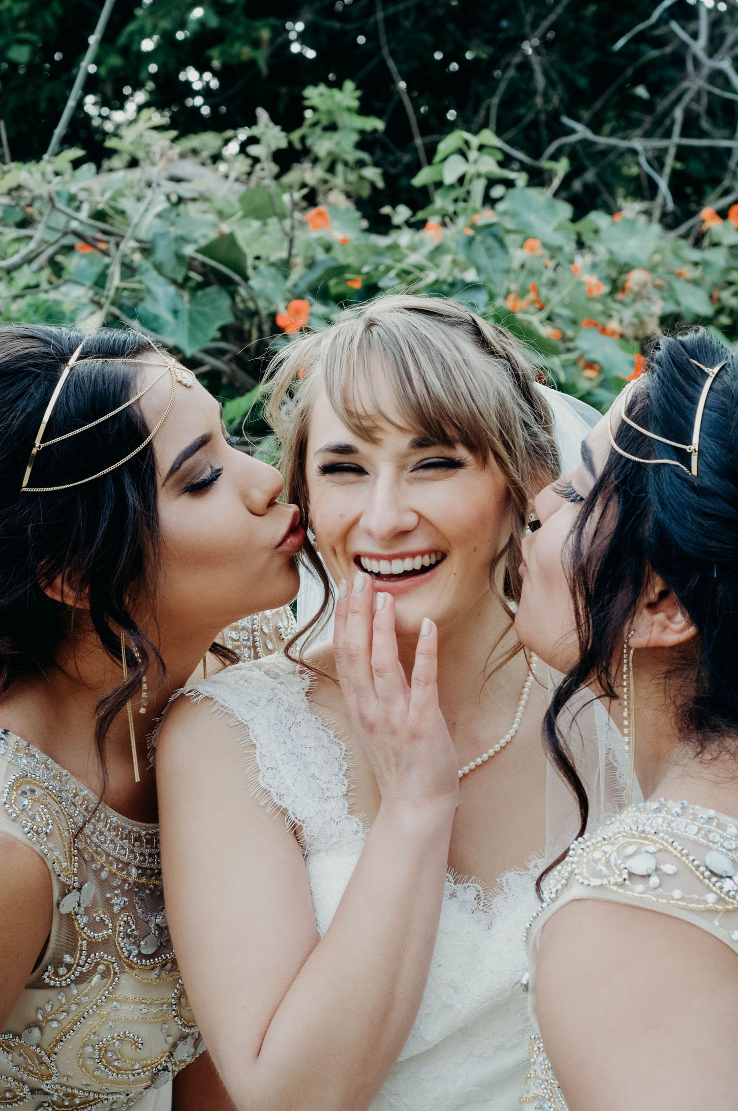 Bride smiles as she's kissed on each cheek by two of her bridesmaids.