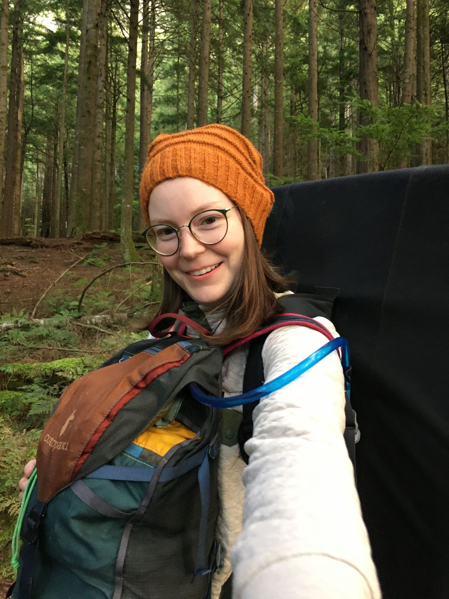Photographer smiles while hiking in a forest with climbing gear.