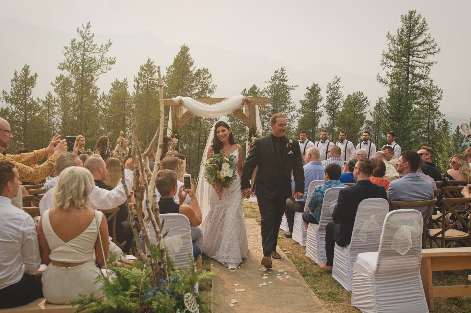 Bride and groom smile as they walk down the aisle together after being married with their guests seated beside them.