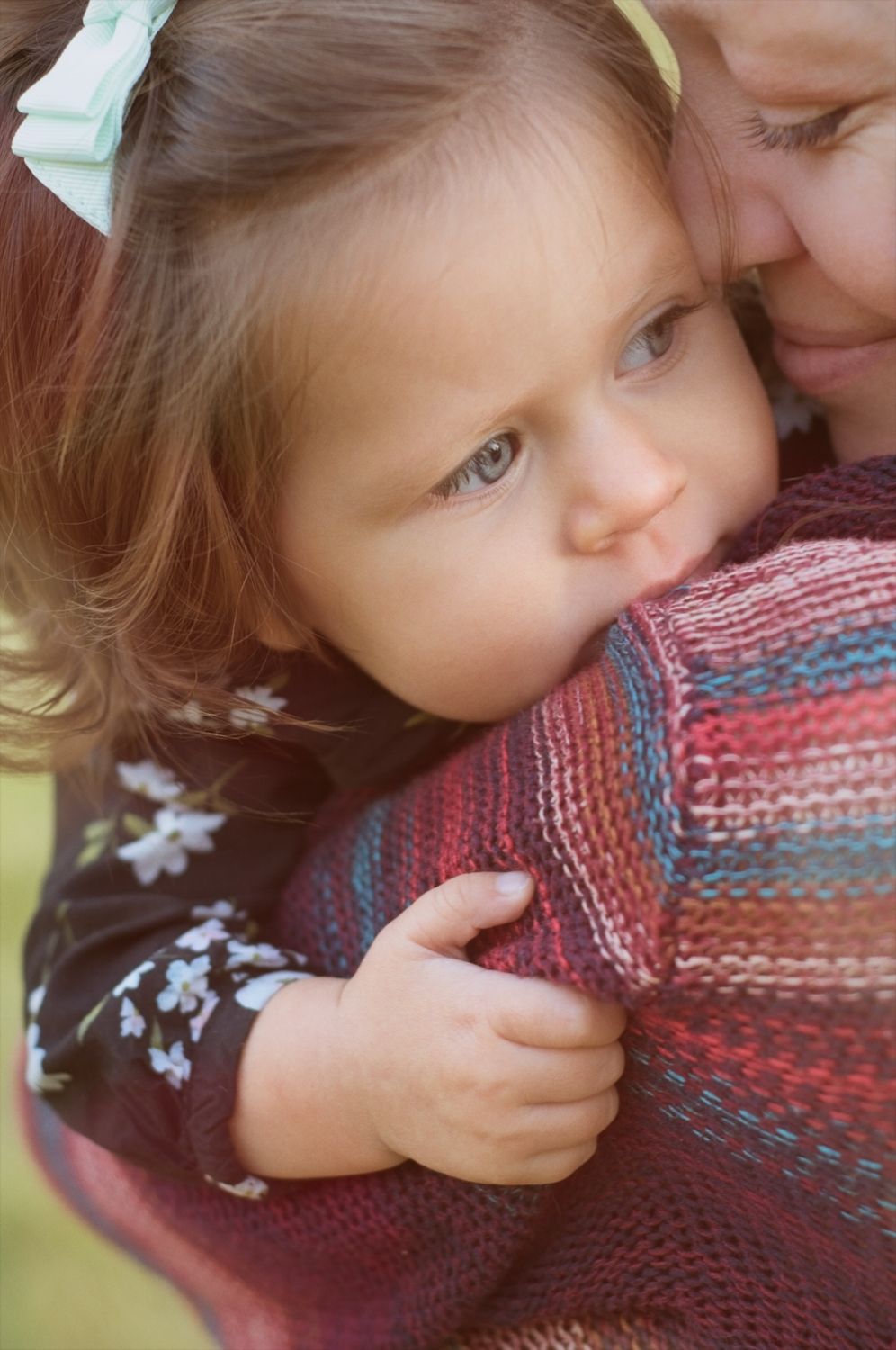 Baby holds on to her mom while being held safely as mom smiles at baby.