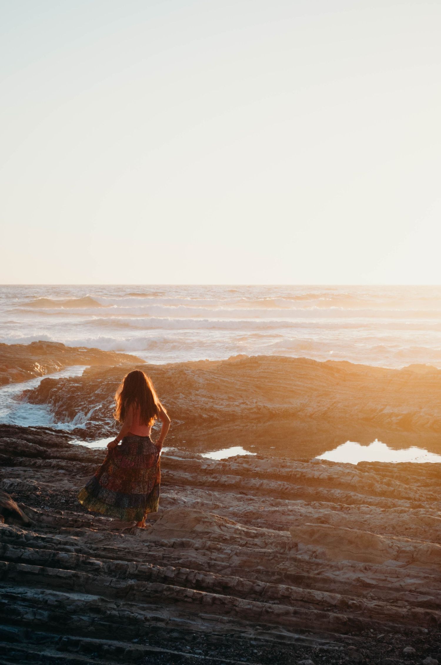 Woman dances on rocks at a beach in California during sunset.