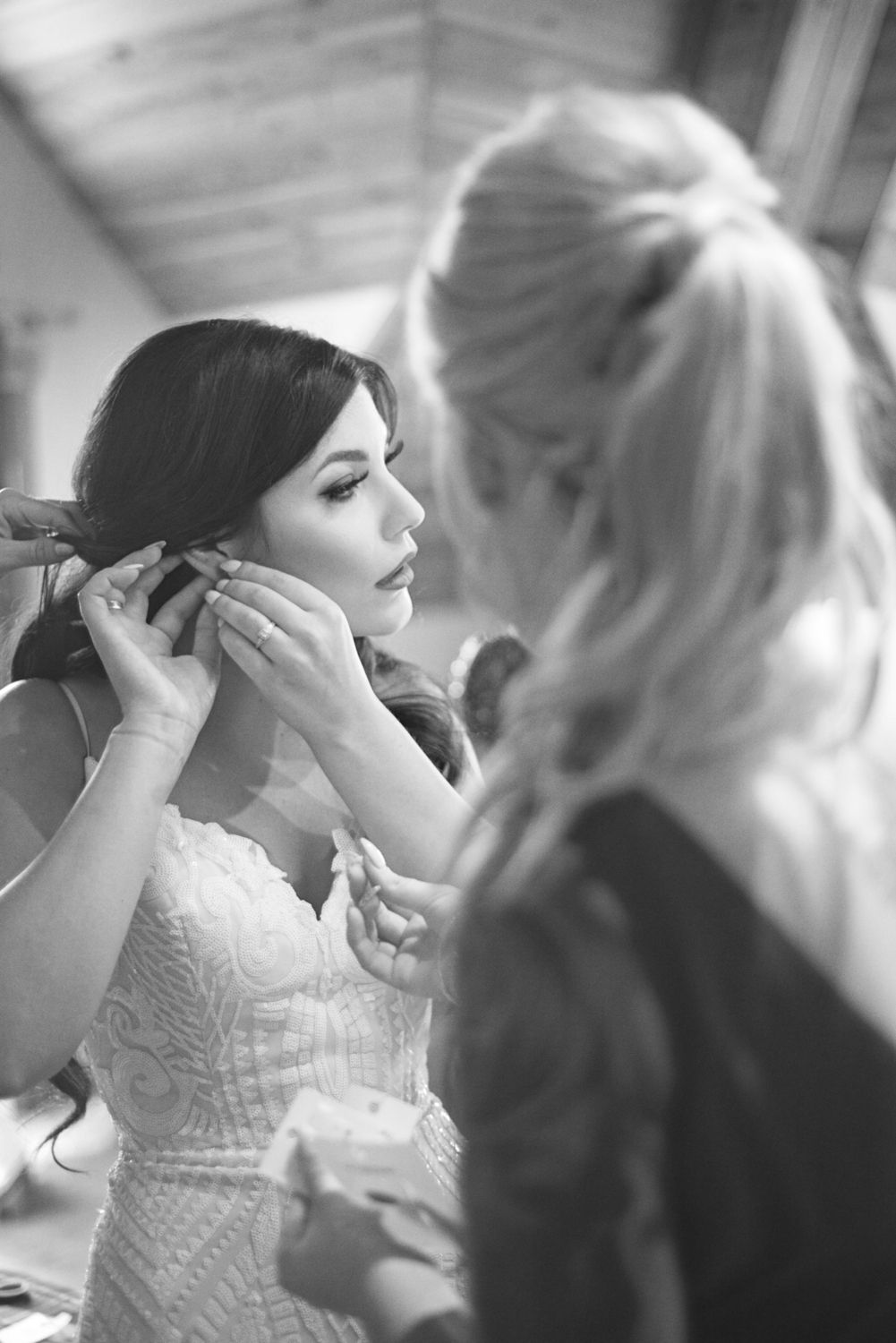 Bride fastens her earrings while getting ready for her wedding ceremony with her bridesmaids.