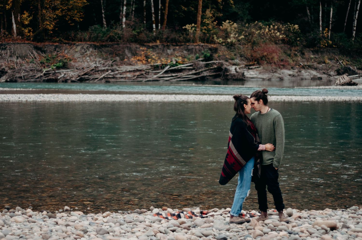 Engaged couple touches foreheads in front of a river.