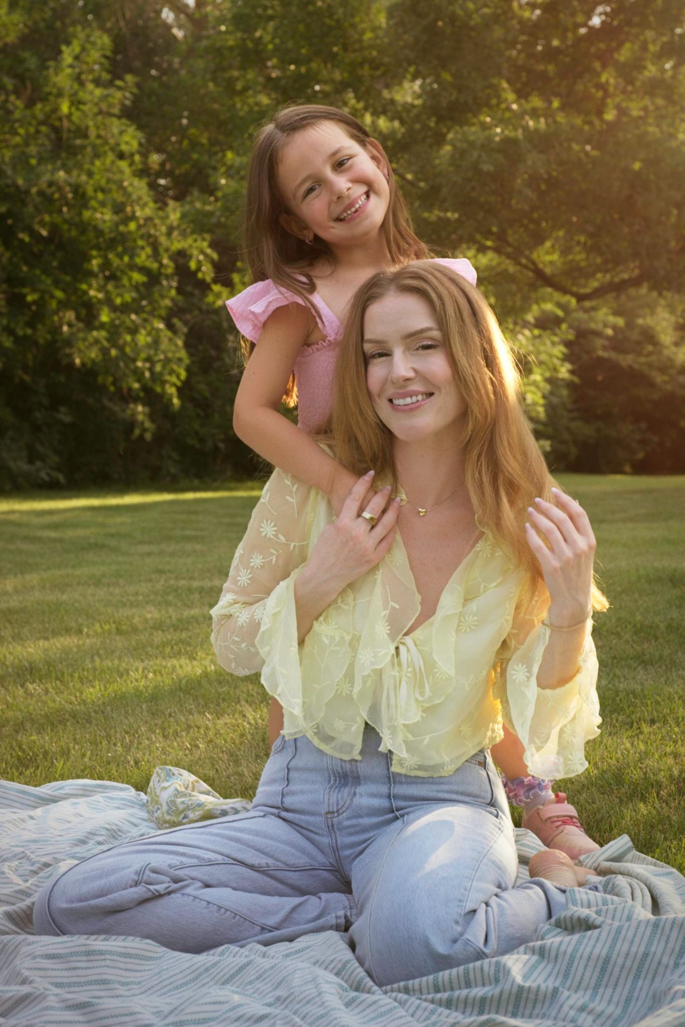 Child standing behind her seated mom smiling beautifully together.