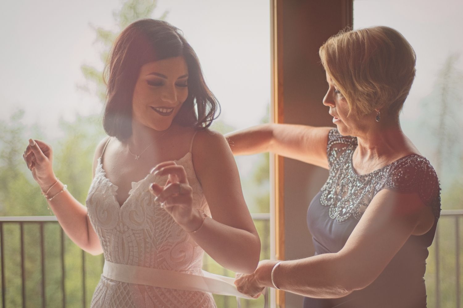 Bride's mother ties the sash around her waist before her wedding ceremony with forest in the background.