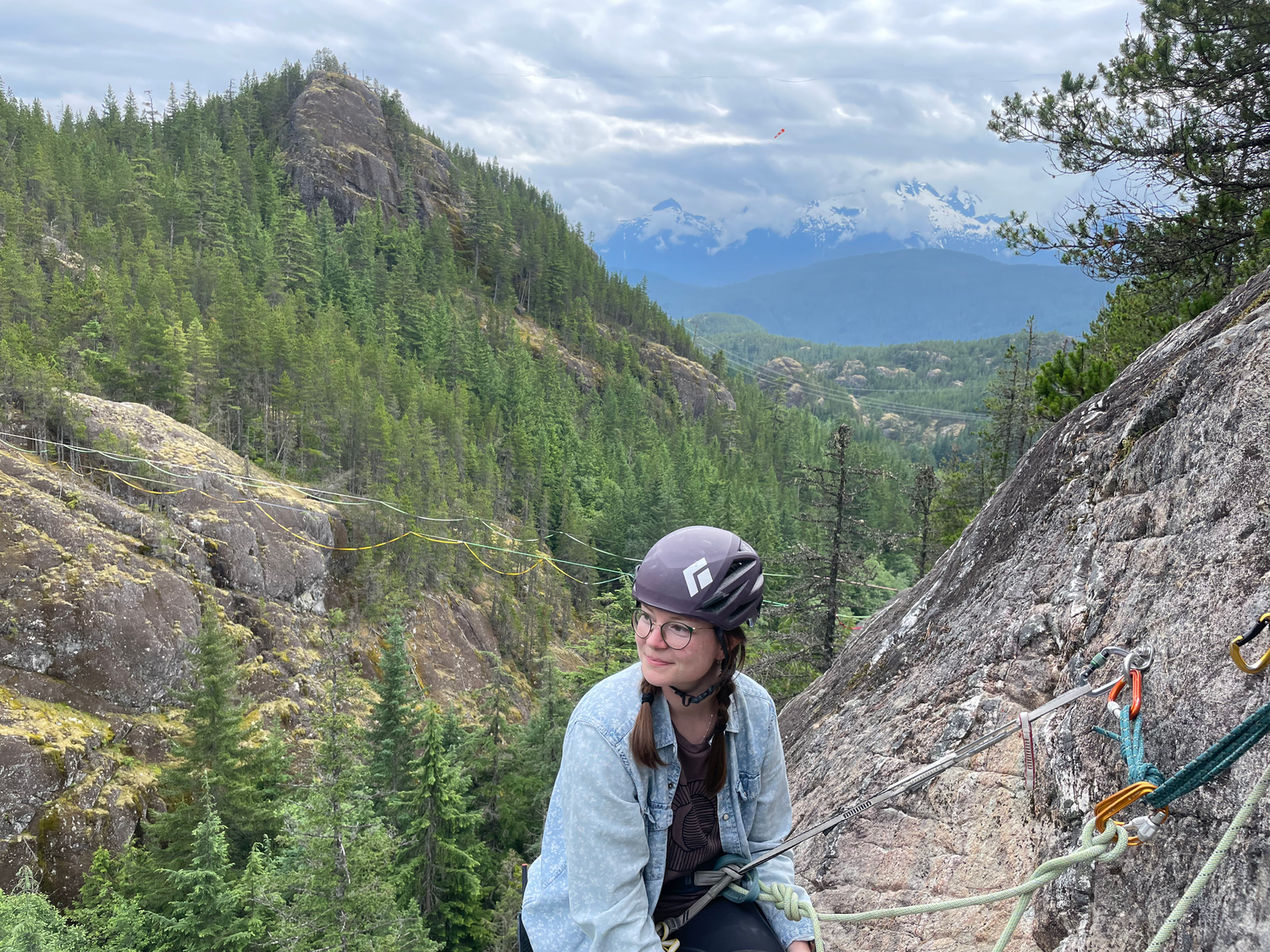 Photographer smiles while taking a break from rock climbing in Squamish, BC with mountains in the background.
