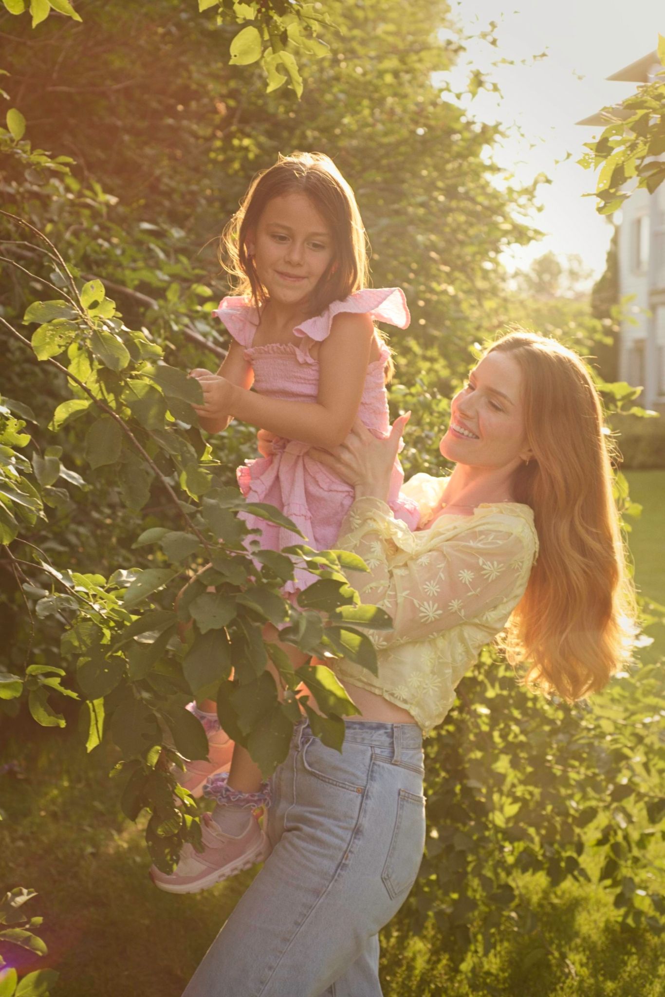 Mom lifting her child to help reach berries in a bush during sunset.