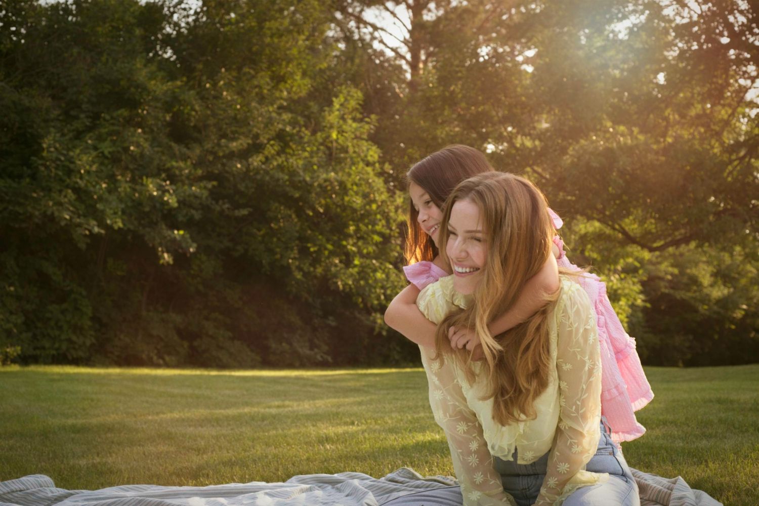 Mother and child laughing together as the child hugs her mom tightly from behind.
