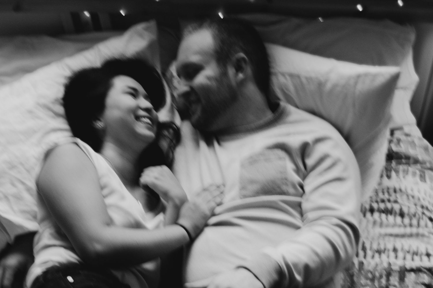 Couple laughs together while snuggling together in bed.