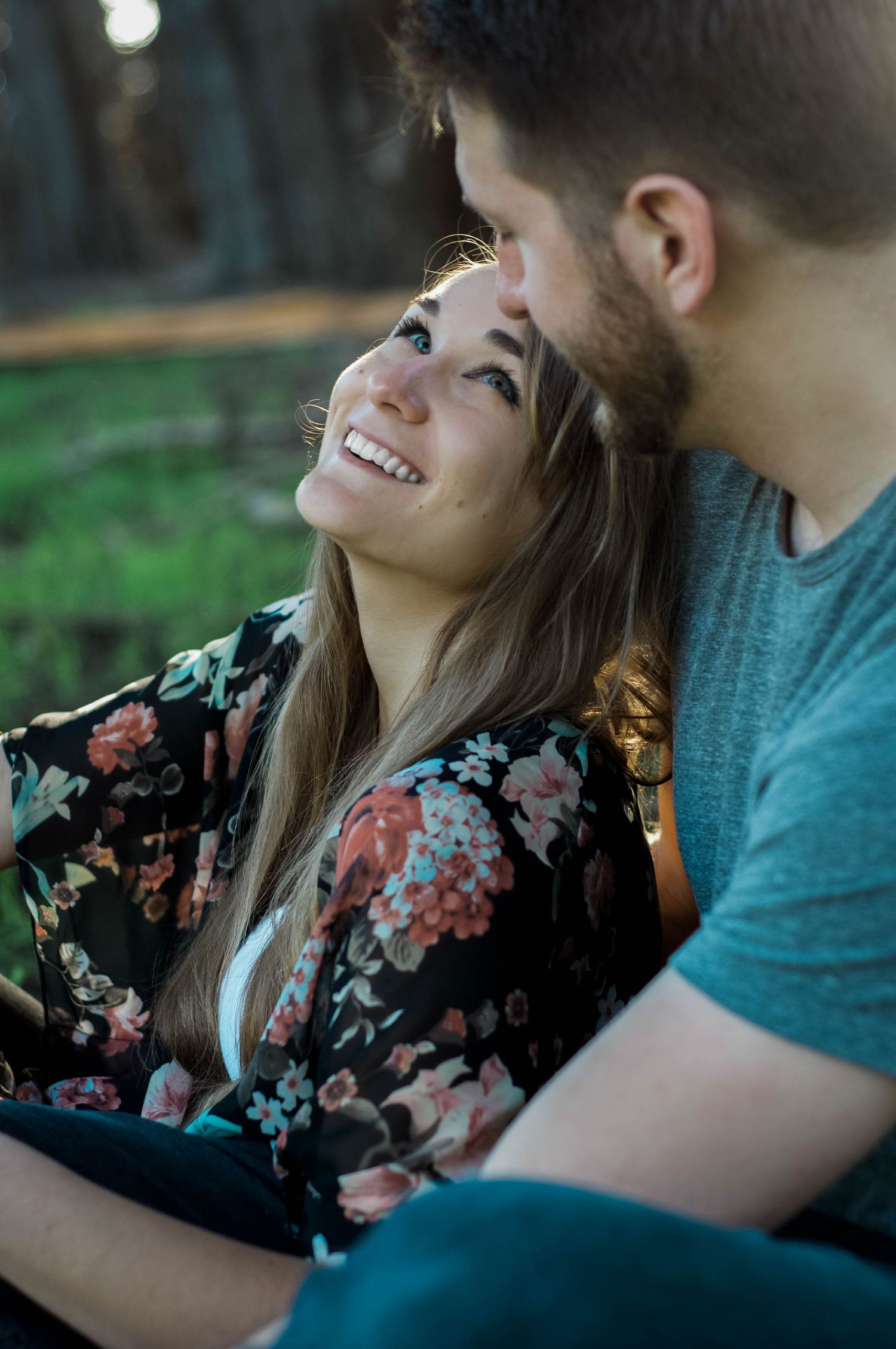 Newly engaged fiancee smiles and looks up at her partner while wrapped in his arms.
