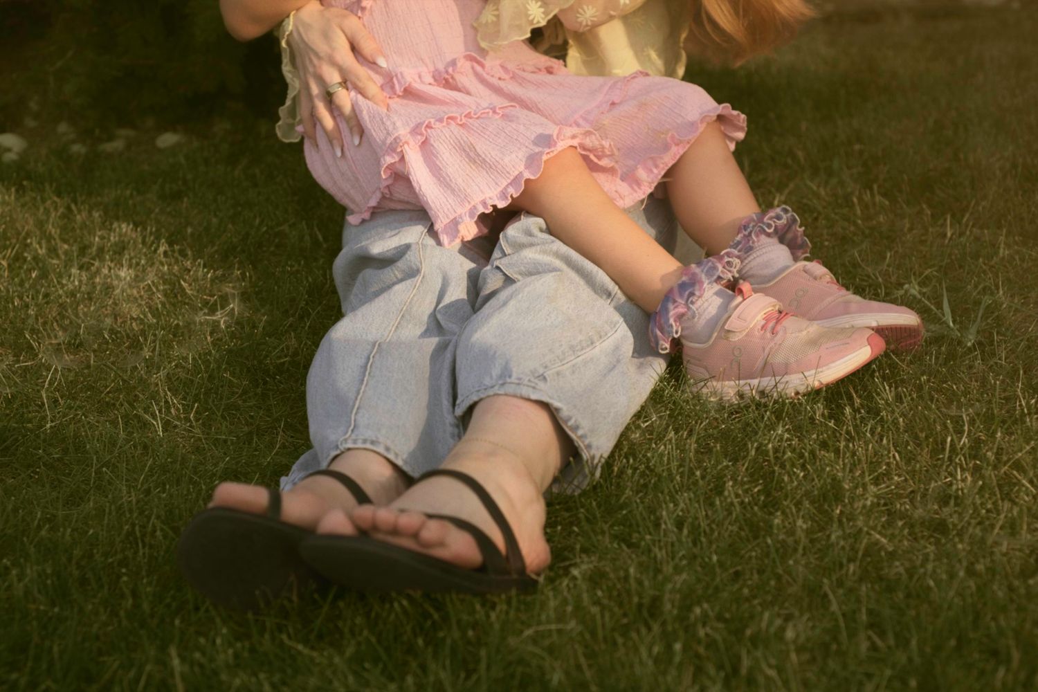 The feet and legs of mother and child while the child sits in her mom's lap.