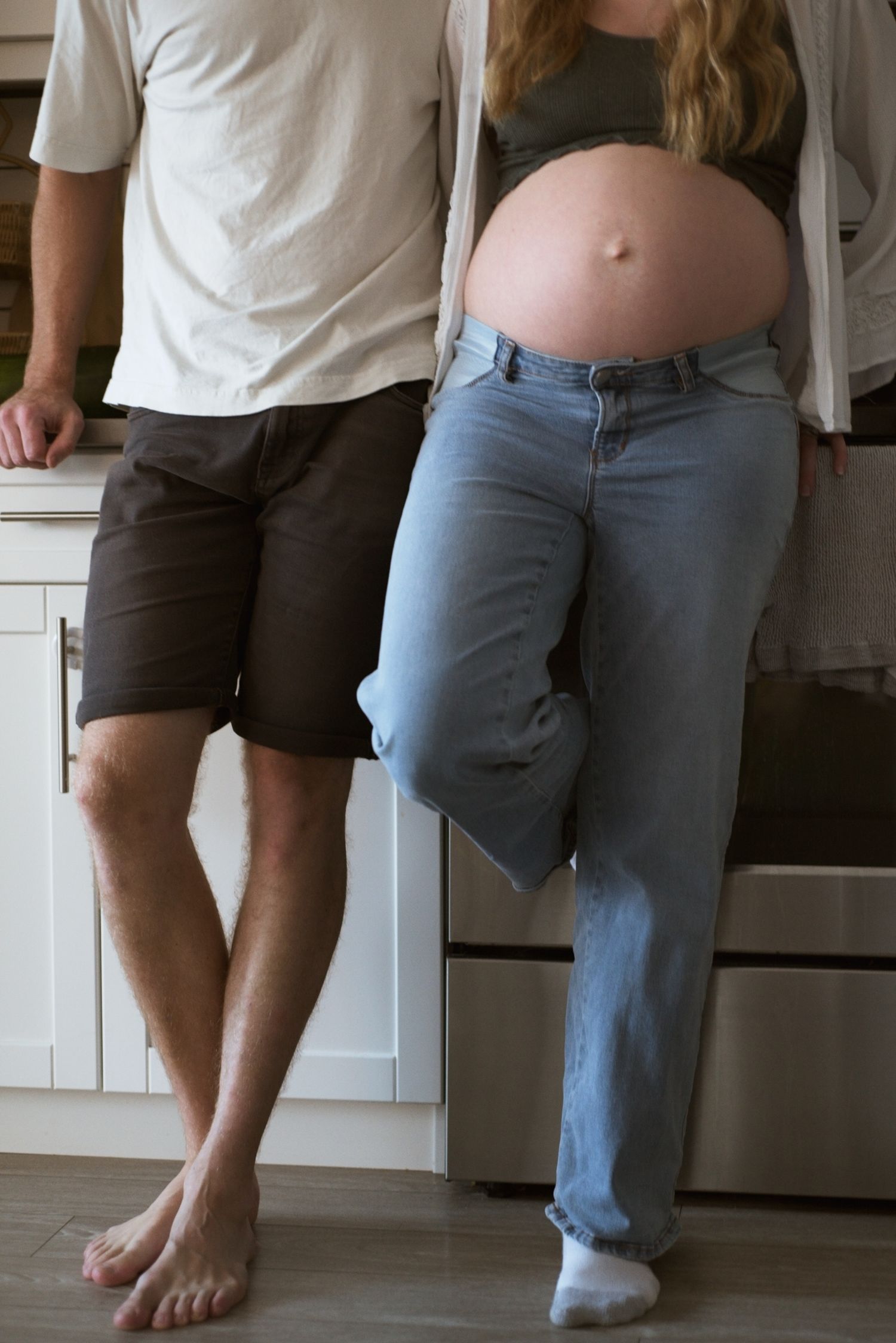 Husband and wife stand together in the kitchen, showing wife's pregnant belly.