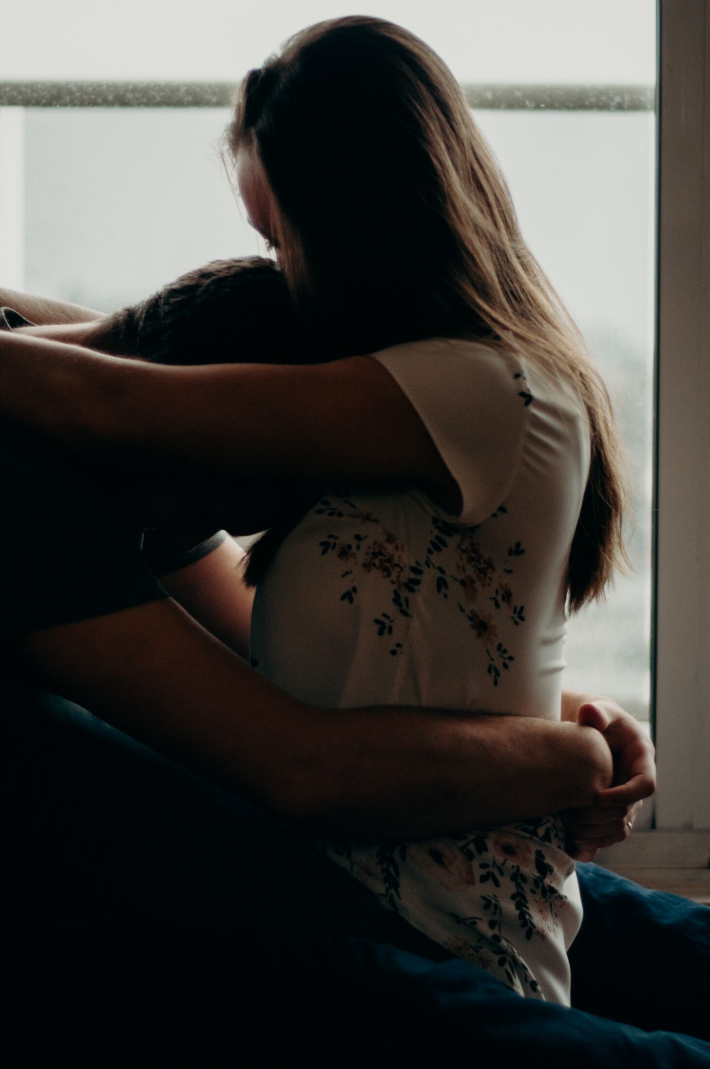 Couple embraces intimately on a rainy day in their home.