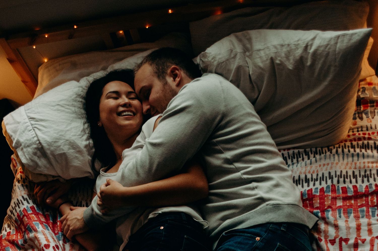Couple cuddled up together smiling in their bed.