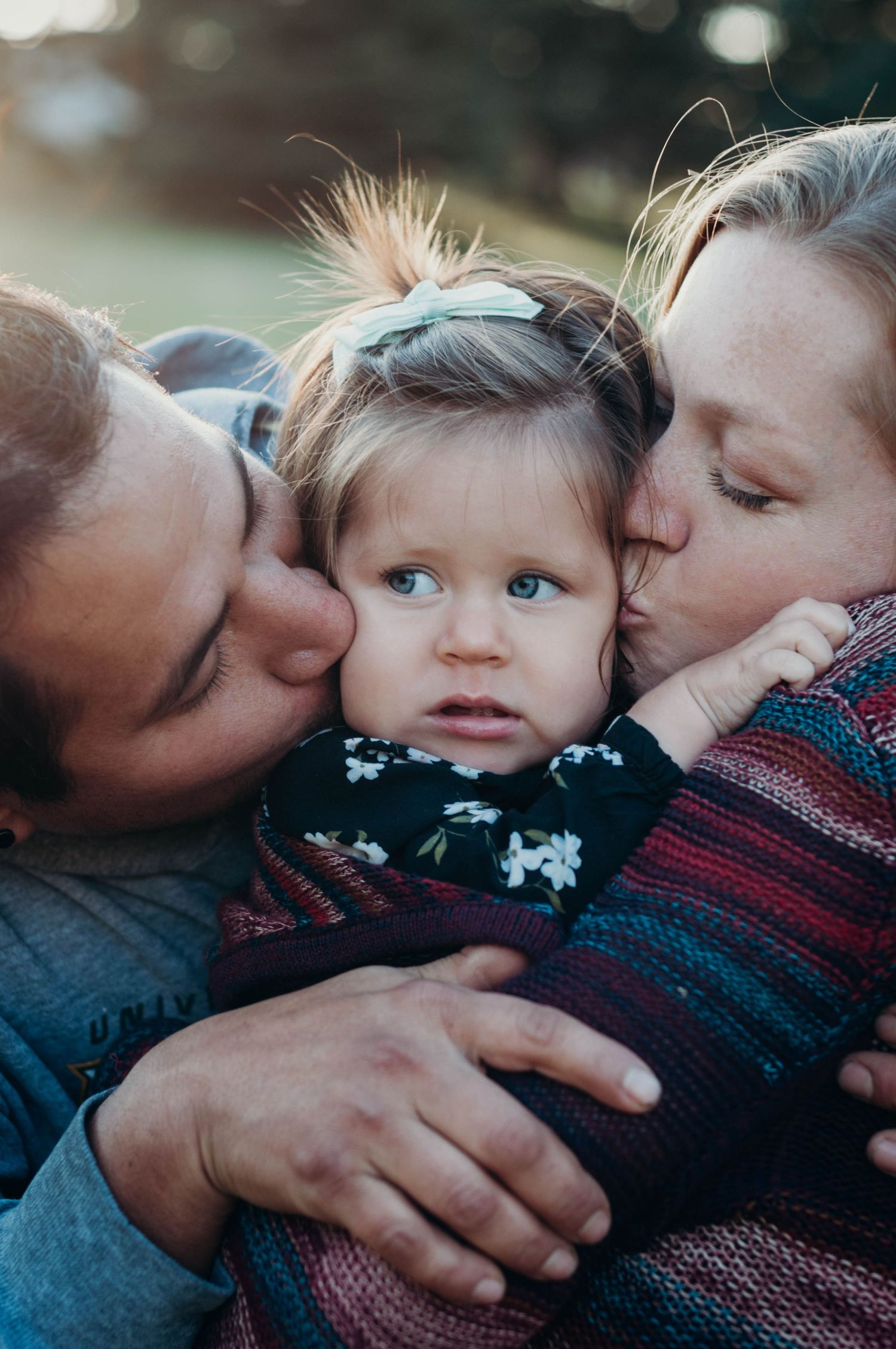 Mom and dad kiss baby's cheeks.