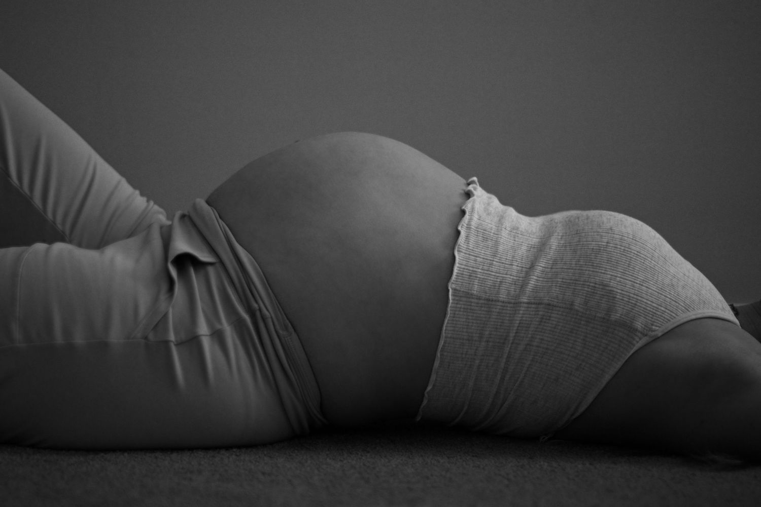 Pregnant woman lies on her back showing the curves of her belly.