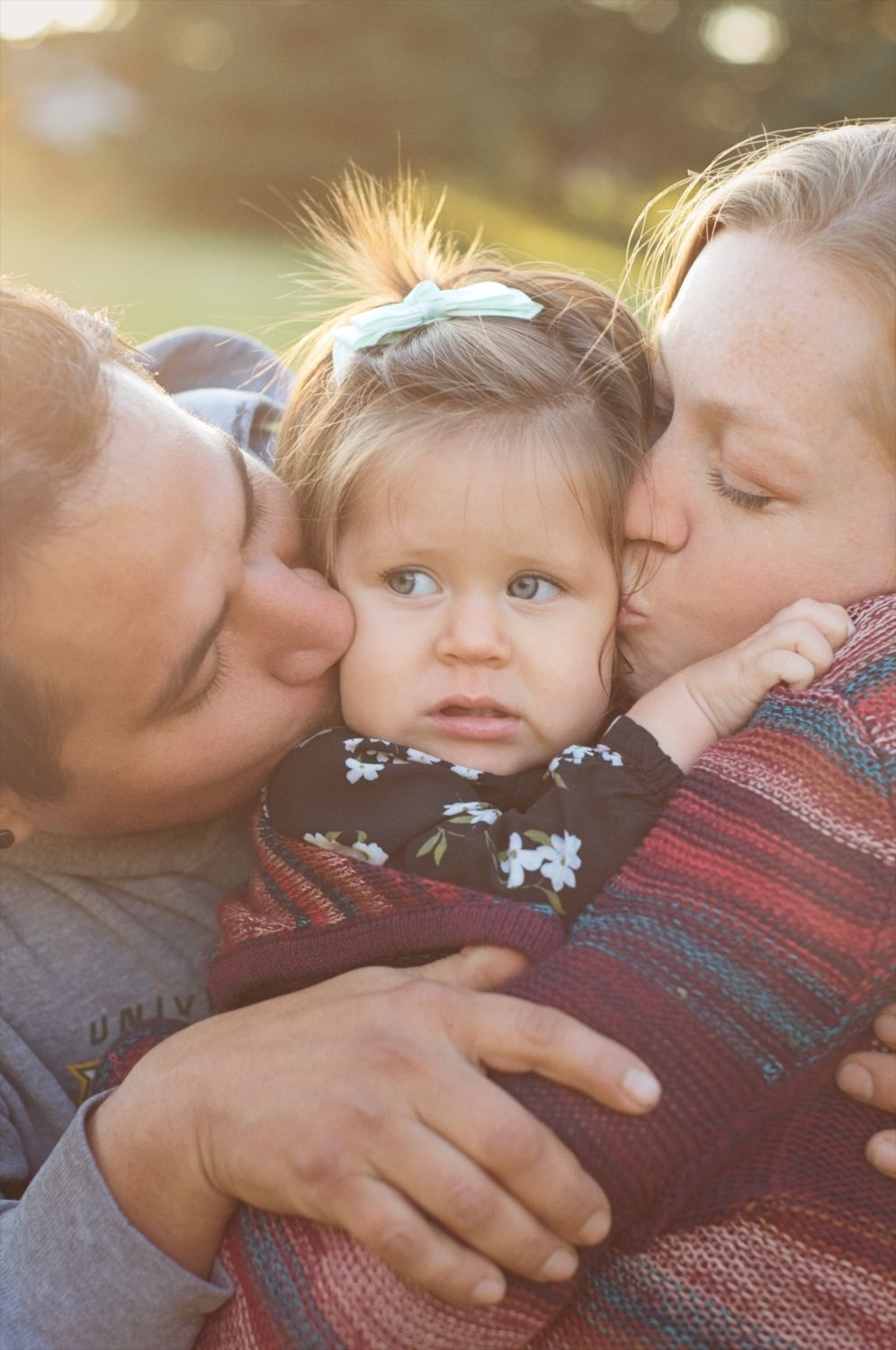 Baby's face is squished while she's kissed on both cheeks by mom and dad.