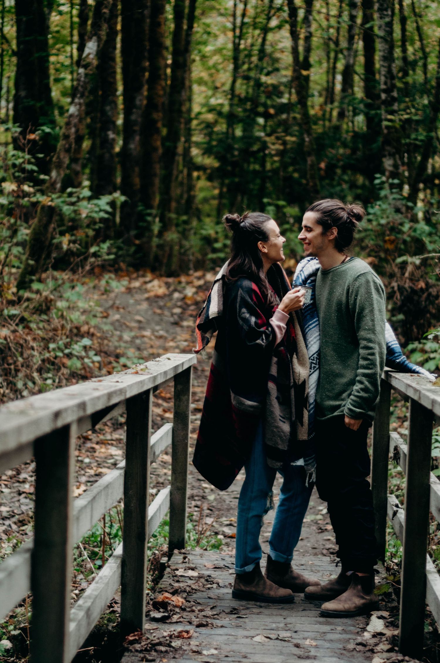 Newly engaged couple stand together on a bridge in a forested area.