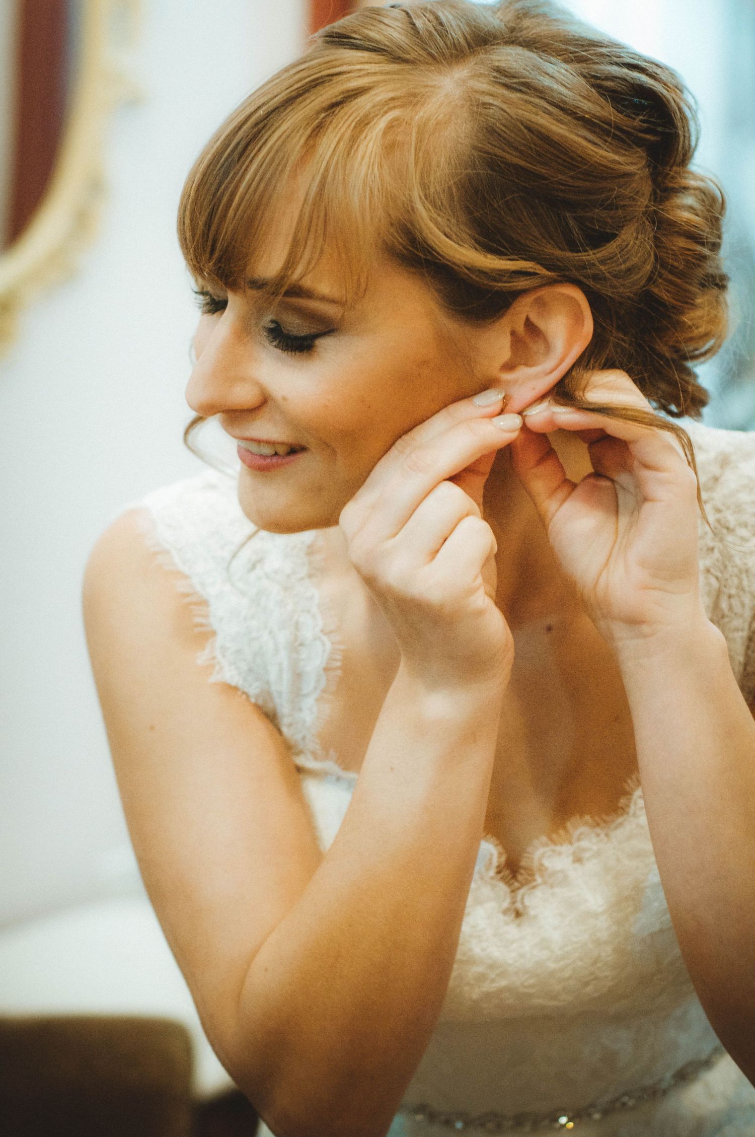 Bride fastening her earrings while getting ready before her wedding day begins.