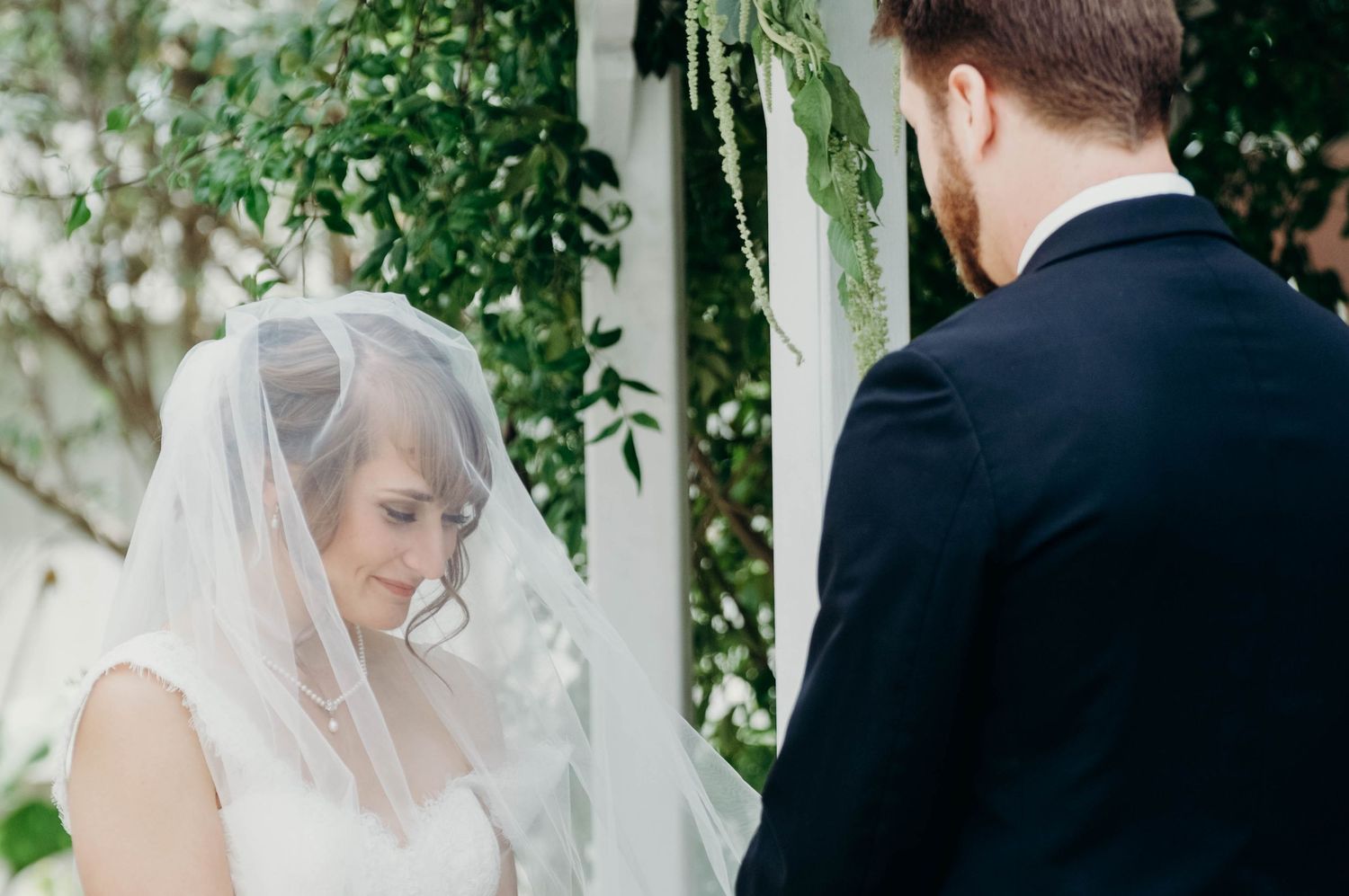 Bride under her veil holds hands with her groom as they exchange vows during the ceremony.