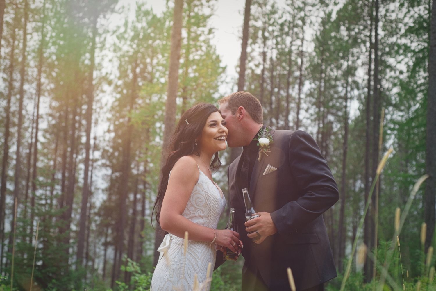 Groom whispers in to the ear of his bride before their wedding reception with trees in the background.