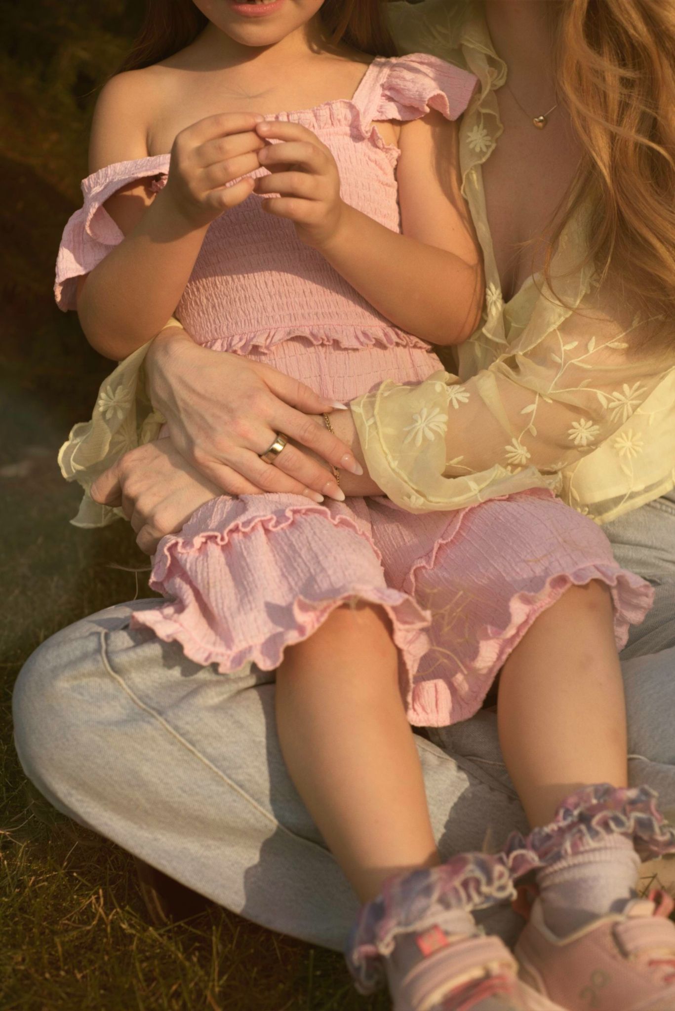 Child sits in her mom's lap while inspecting a dandelion.