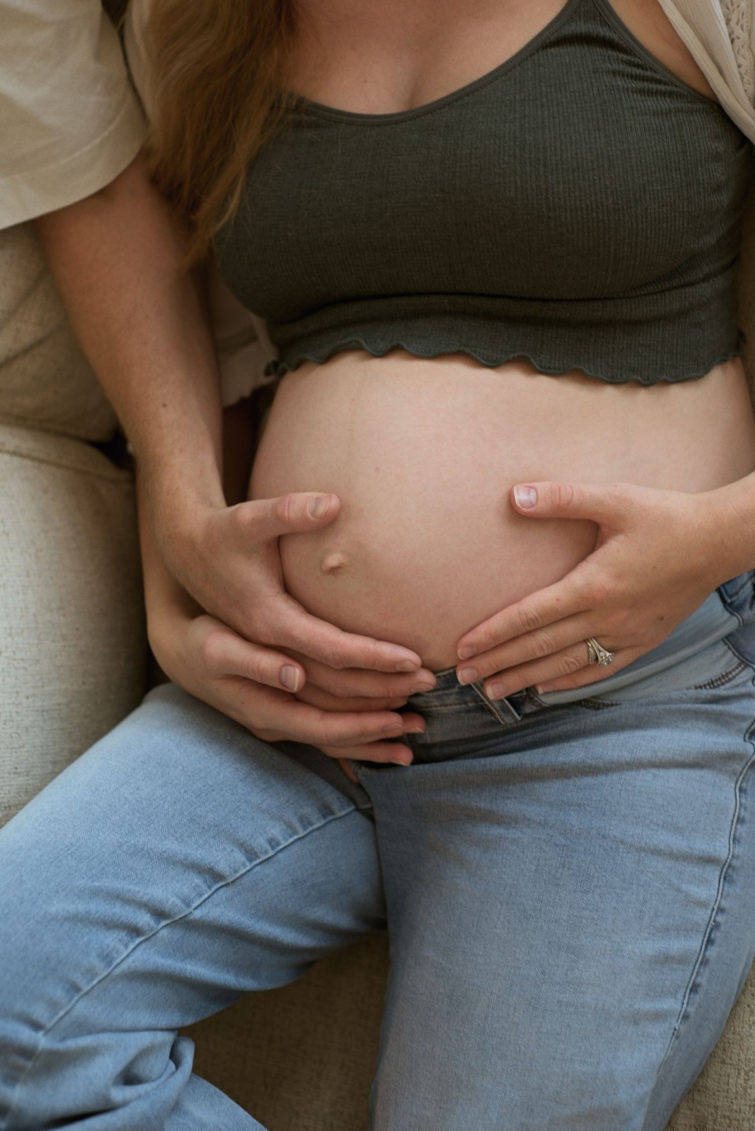 Wife's pregnant belly is cradled by her and her husband's hand as they snuggle.