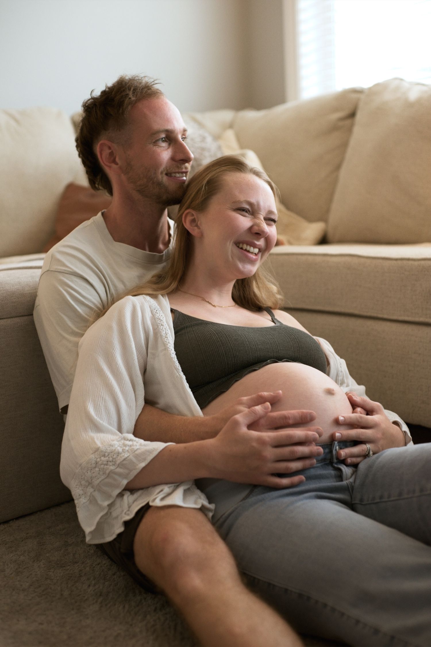 Dad sits behind his pregnant wife as they smile.