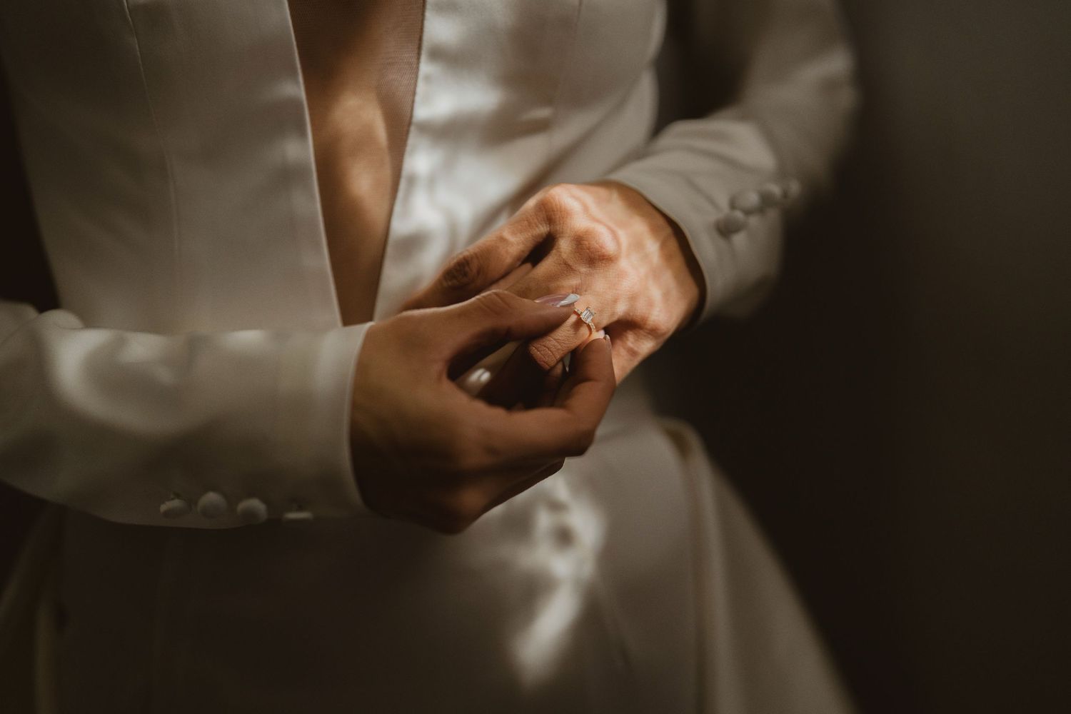 Close-up of bride and groom exchanging wedding rings in elegant white attire.