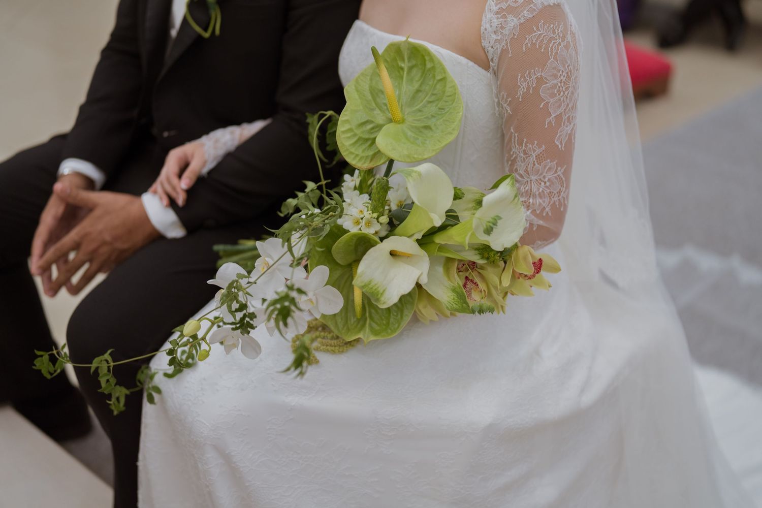 Close-up of bride holding cascading green and white wedding bouquet with anthuriums and calla lilies.