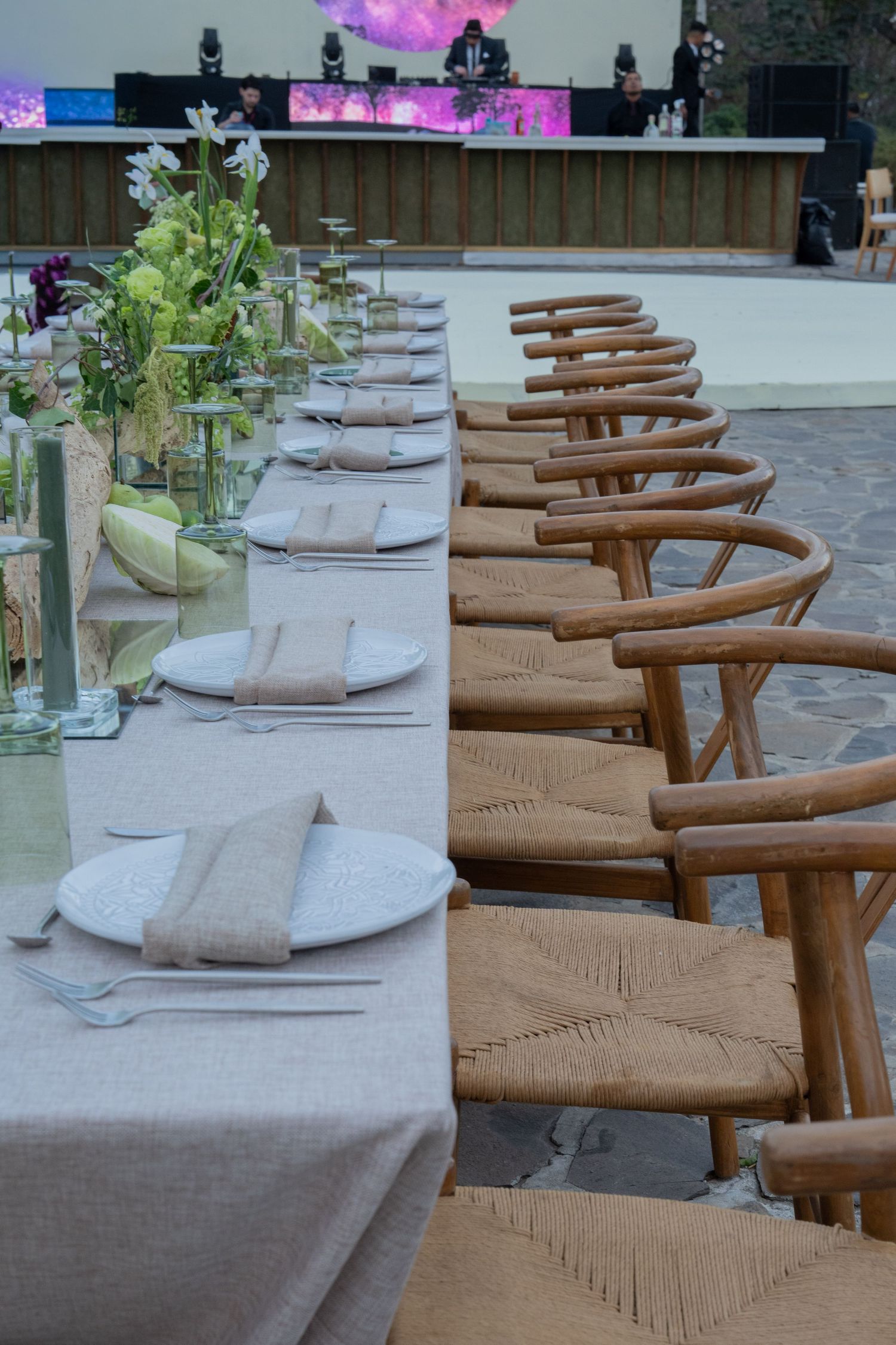 Elegant outdoor wedding reception table set with linen napkins, white plates, and wooden chairs.