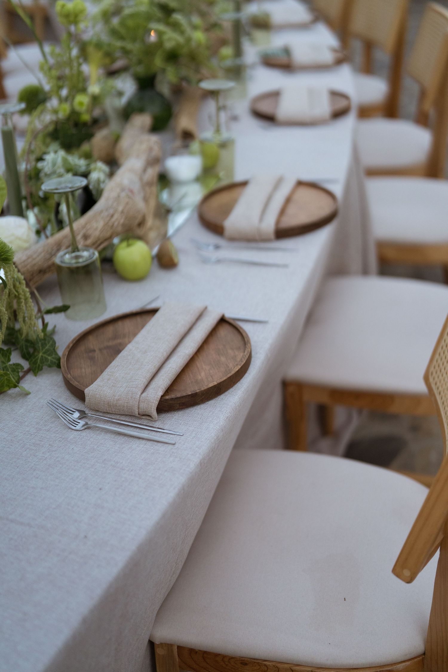 Rustic wedding table setting with wooden charger plates, linen napkins, and green apple centerpieces.