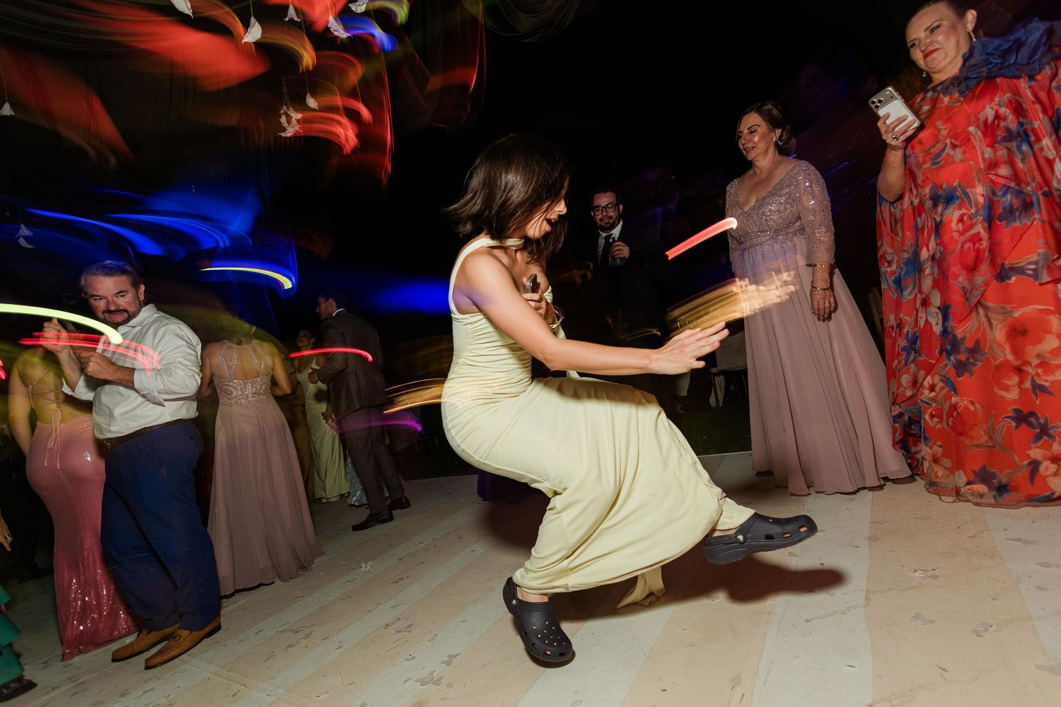Wedding guest in a yellow dress dancing energetically with glow sticks at a festive wedding reception.