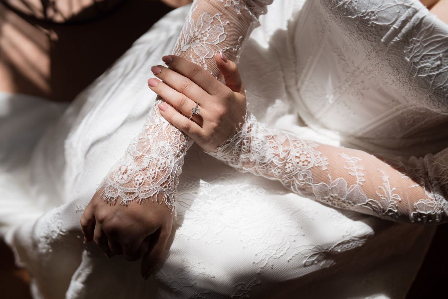 Close-up of bride's hands in delicate lace wedding dress sleeves with gold ring.