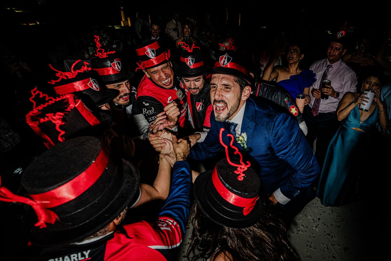 Groom in blue suit celebrated by mariachi band in red hats at lively wedding reception.