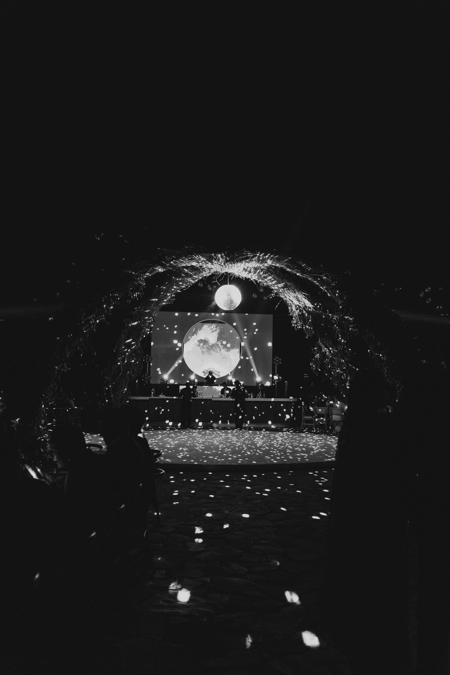 Black and white nighttime wedding reception viewed through arch with confetti falling on dance floor.