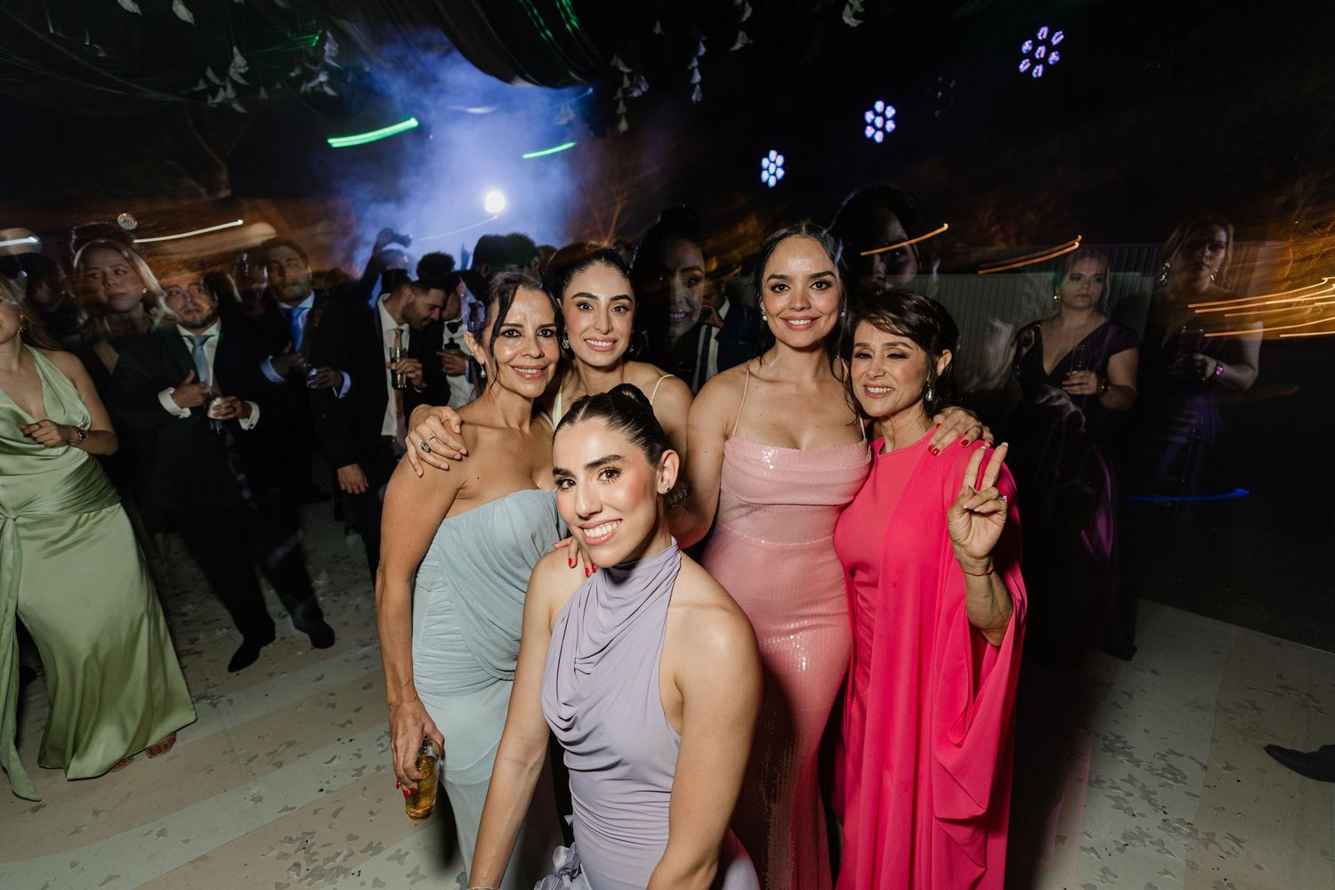Five women posing together smiling at elegant wedding party.