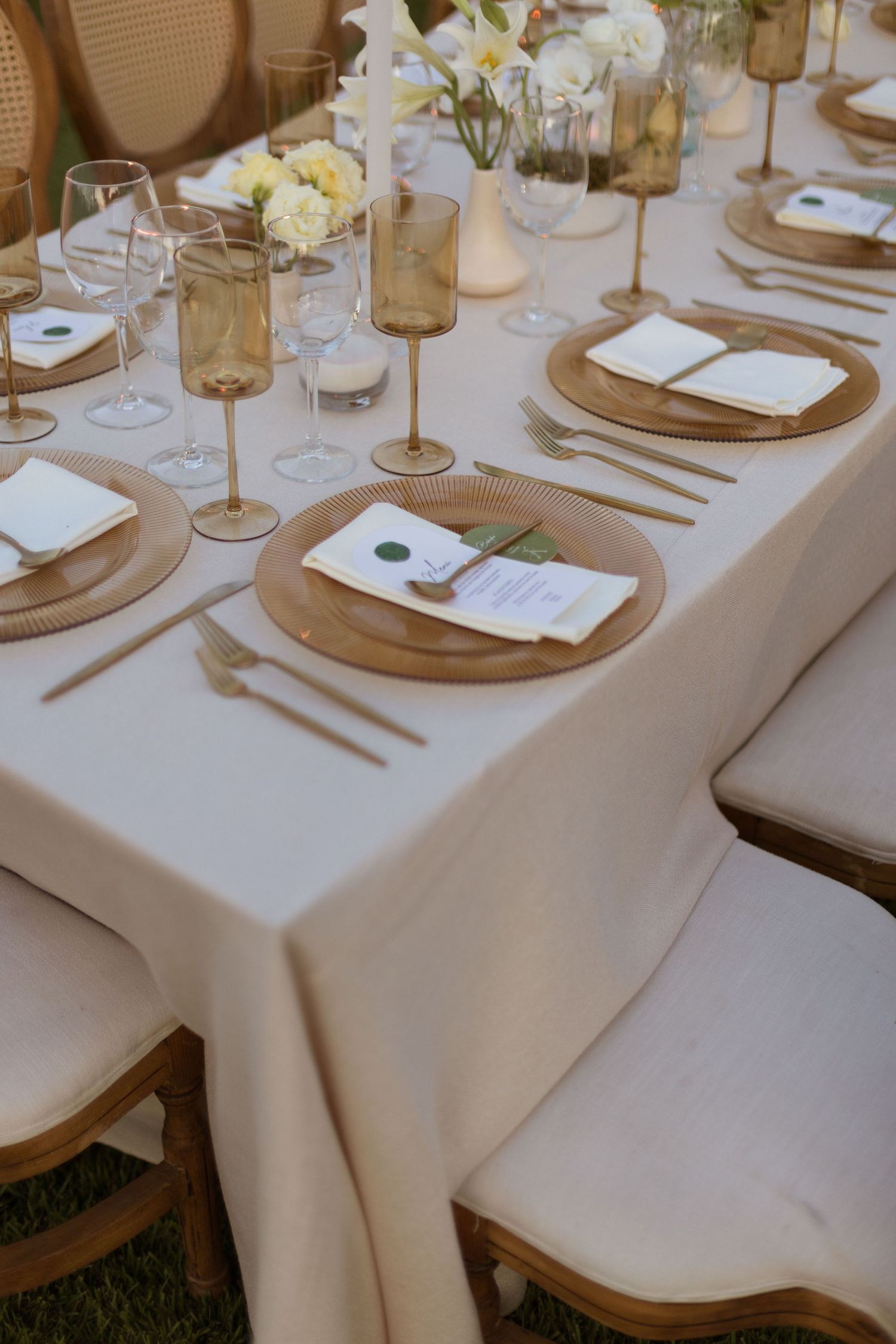 Elegant wedding reception table with gold charger plates, amber glasses, white flowers, and gold cutlery.