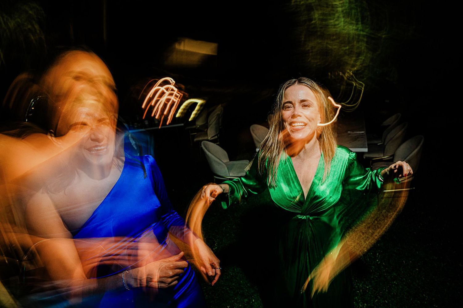 Motion blur photo of women in blue and green dresses dancing at wedding reception.