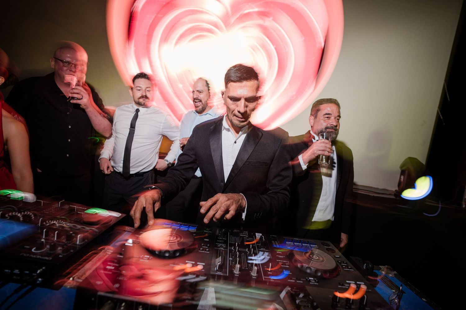DJ performing at wedding reception with heart-shaped light display and guests in background.