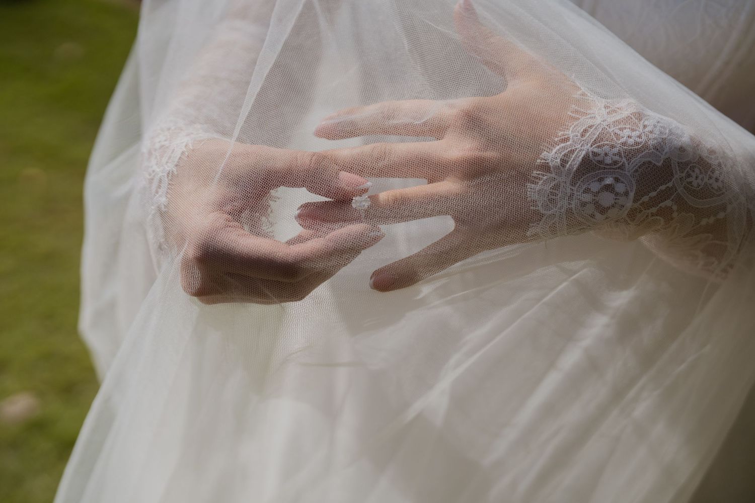Close-up of bride's hands wearing lace gloves and wedding ring over white bridal gown.