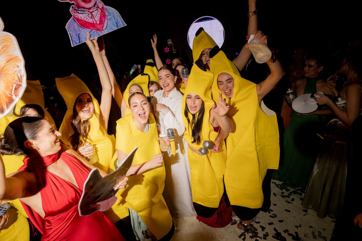 Wedding guests in yellow banana costumes pose with bride for fun photo at themed reception party.