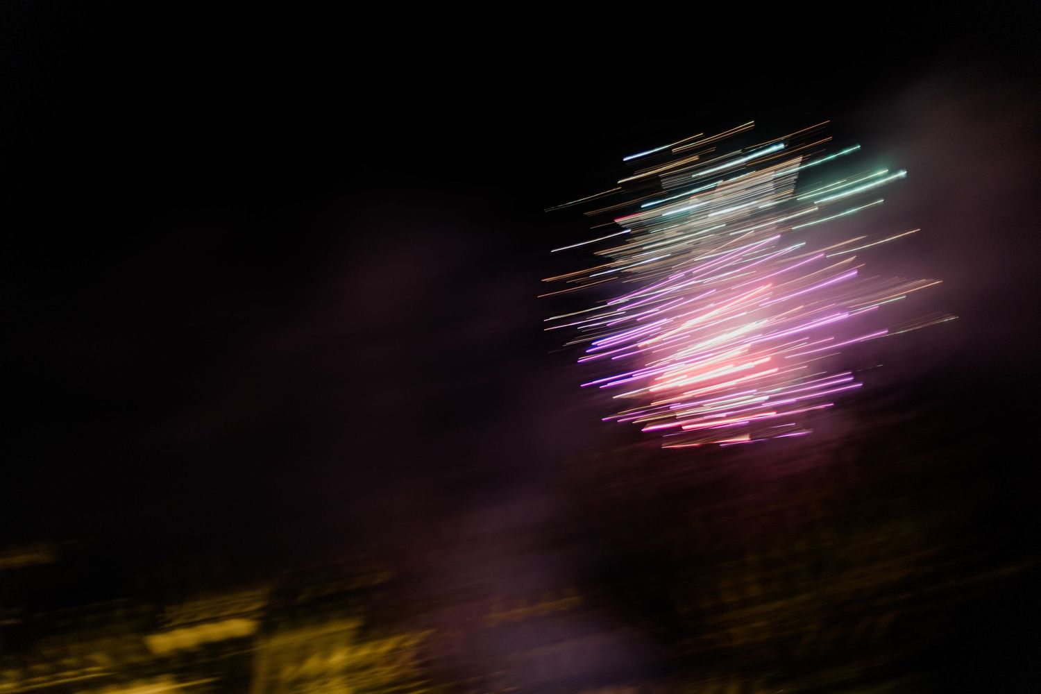 Colorful fireworks display with vibrant pink and green light streaks against a dark night sky.