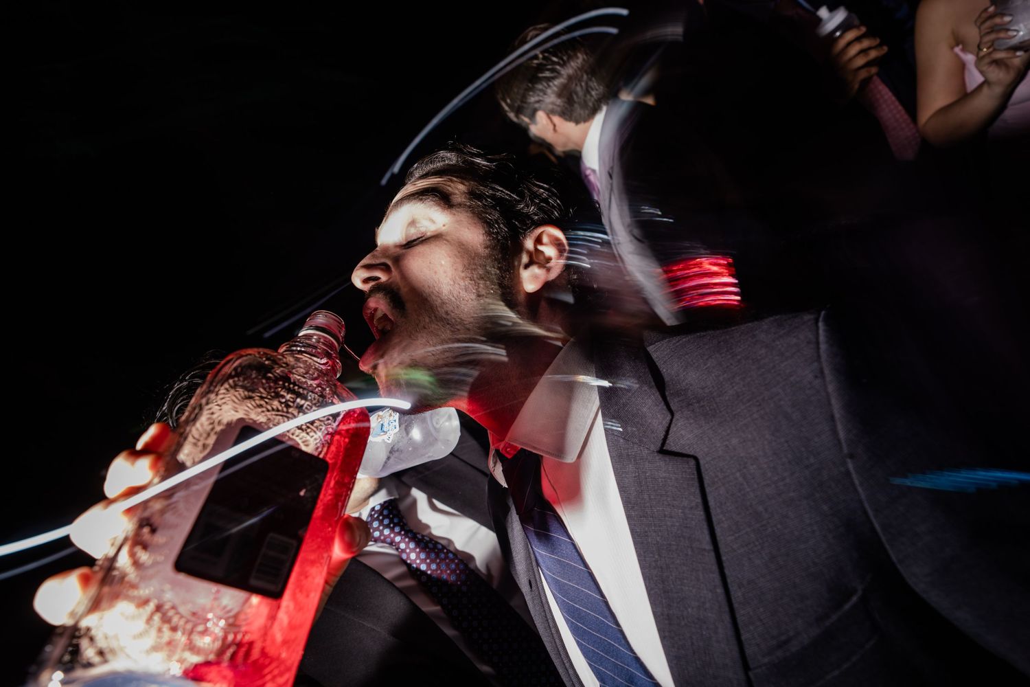 Guest receives playful drink pour at lively wedding reception party in dramatic close-up shot.