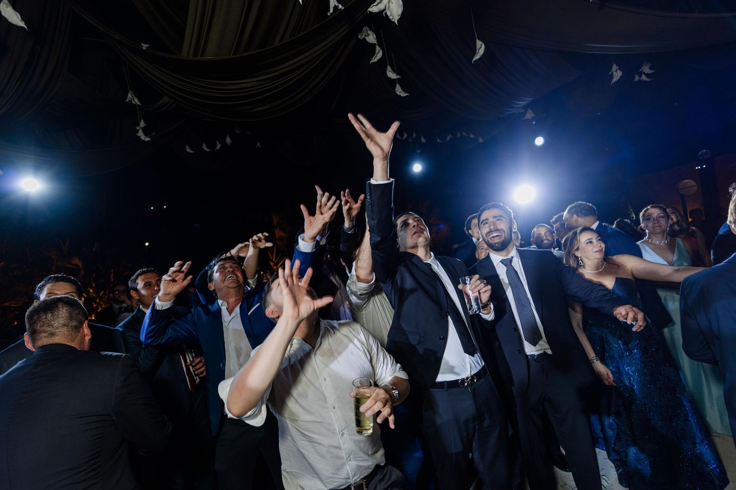 Wedding guests reaching up joyfully on dance floor at reception.