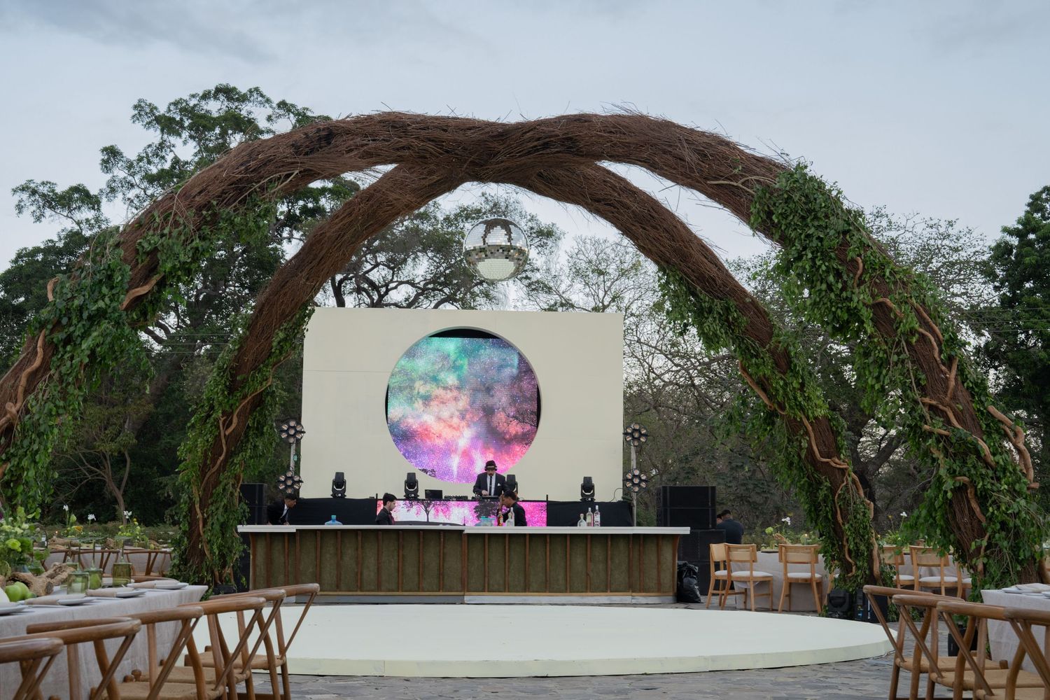 Outdoor wedding venue with rustic wooden arch and circular LED screen stage setup.